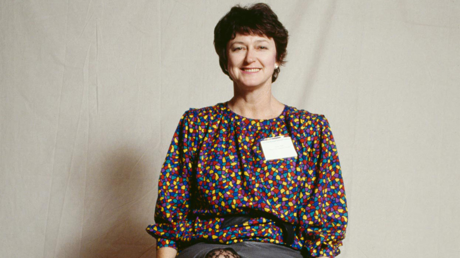 Older image of Susan Ryan, she has short brown hair with a loose multicoloured spotted top. 