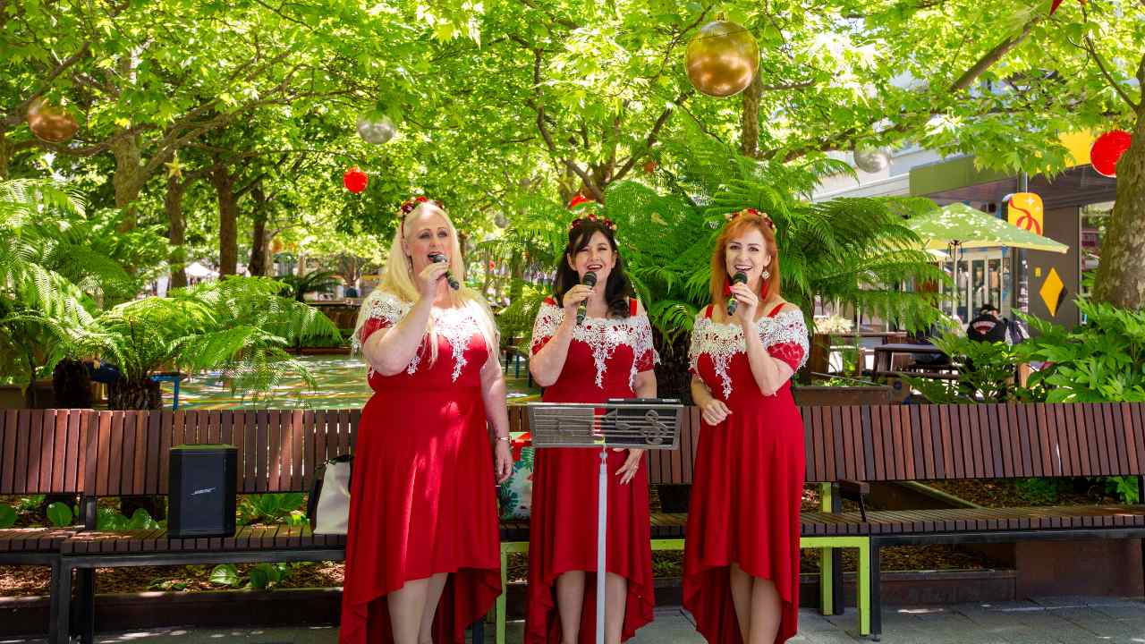 Three women standing amongst decorations singing.