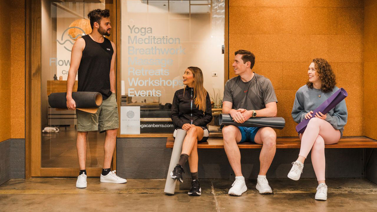 Four young people outside a yoga studio holding yoga mats