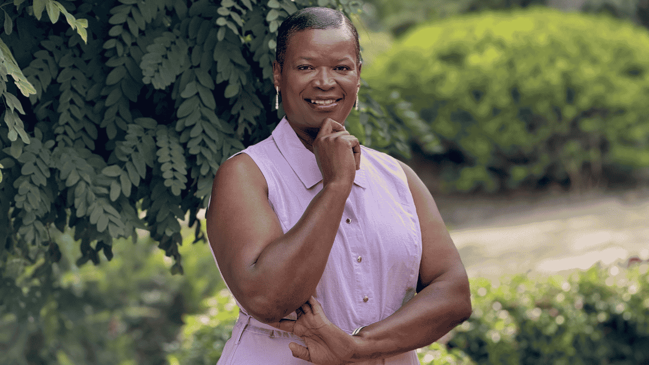 A person smiling with their arms crossed in front of a tree.