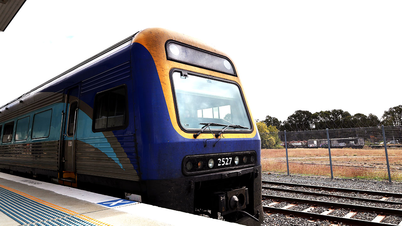 A blue and yellow train stopped at a station on a foggyday.