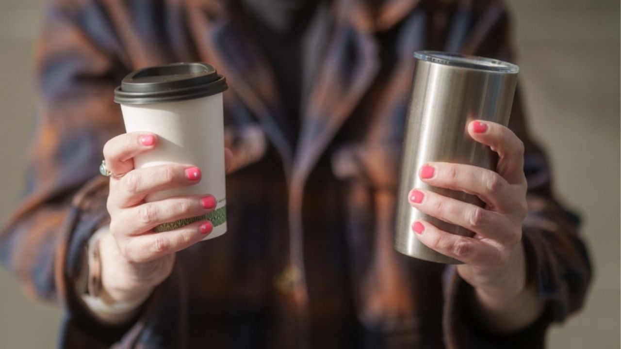 A person holds reusable and disposable coffee cups