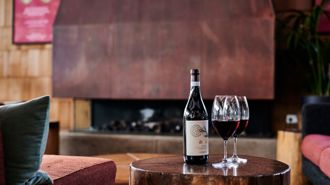 A bottle of red wine and two half-filled glasses in front of a modern fireplace in a bar.