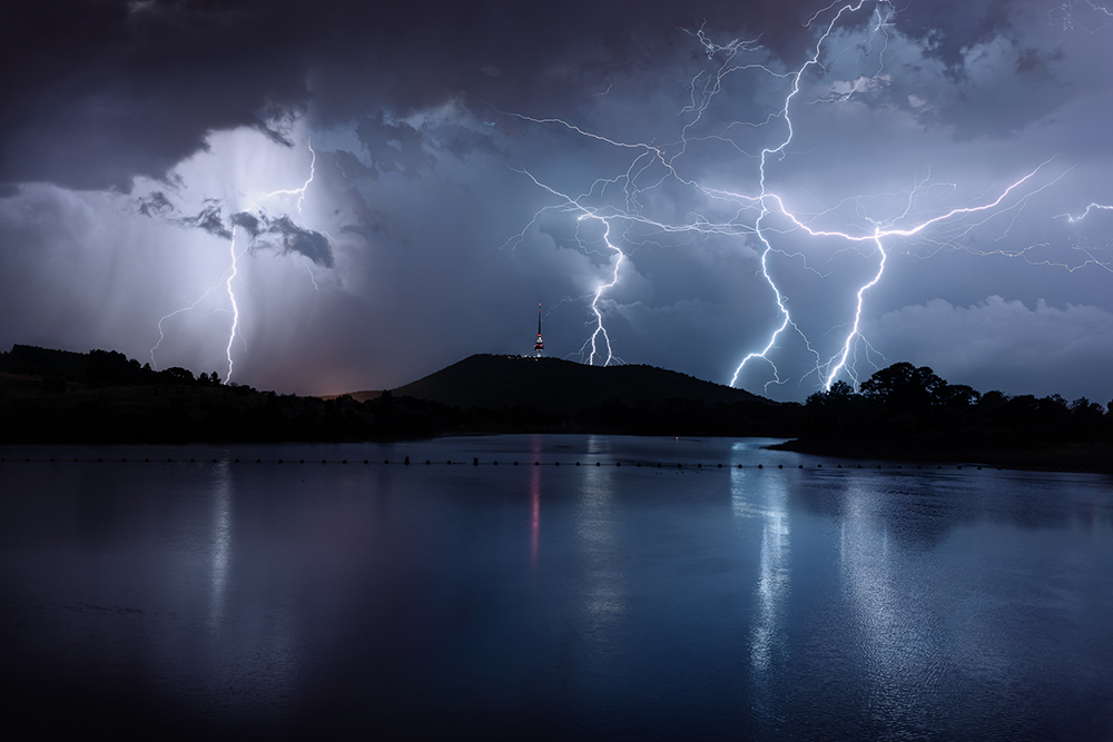 Lightning surrounds a tower on a hill.