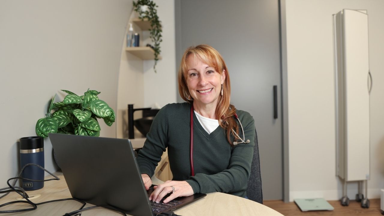 Person with a stethoscope using a laptop at a desk in a modern office.