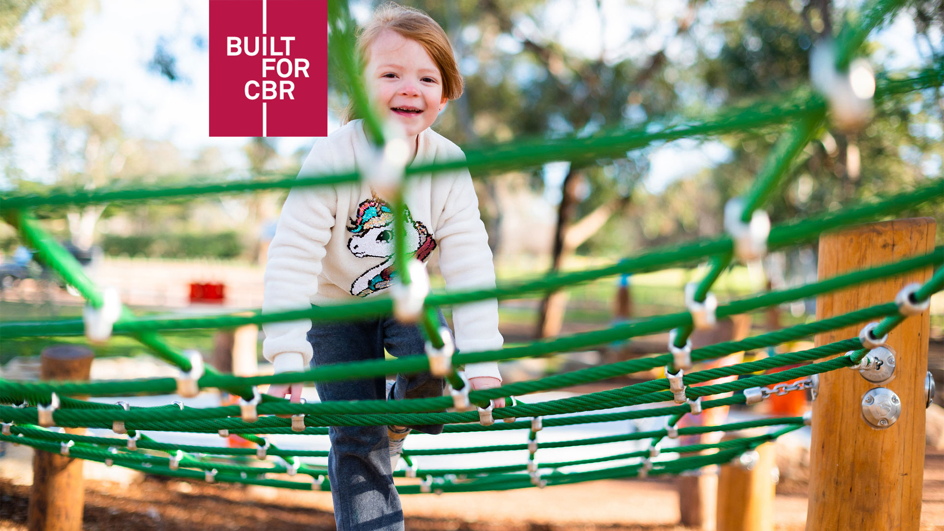 A smiling child climbs across netting at a playground