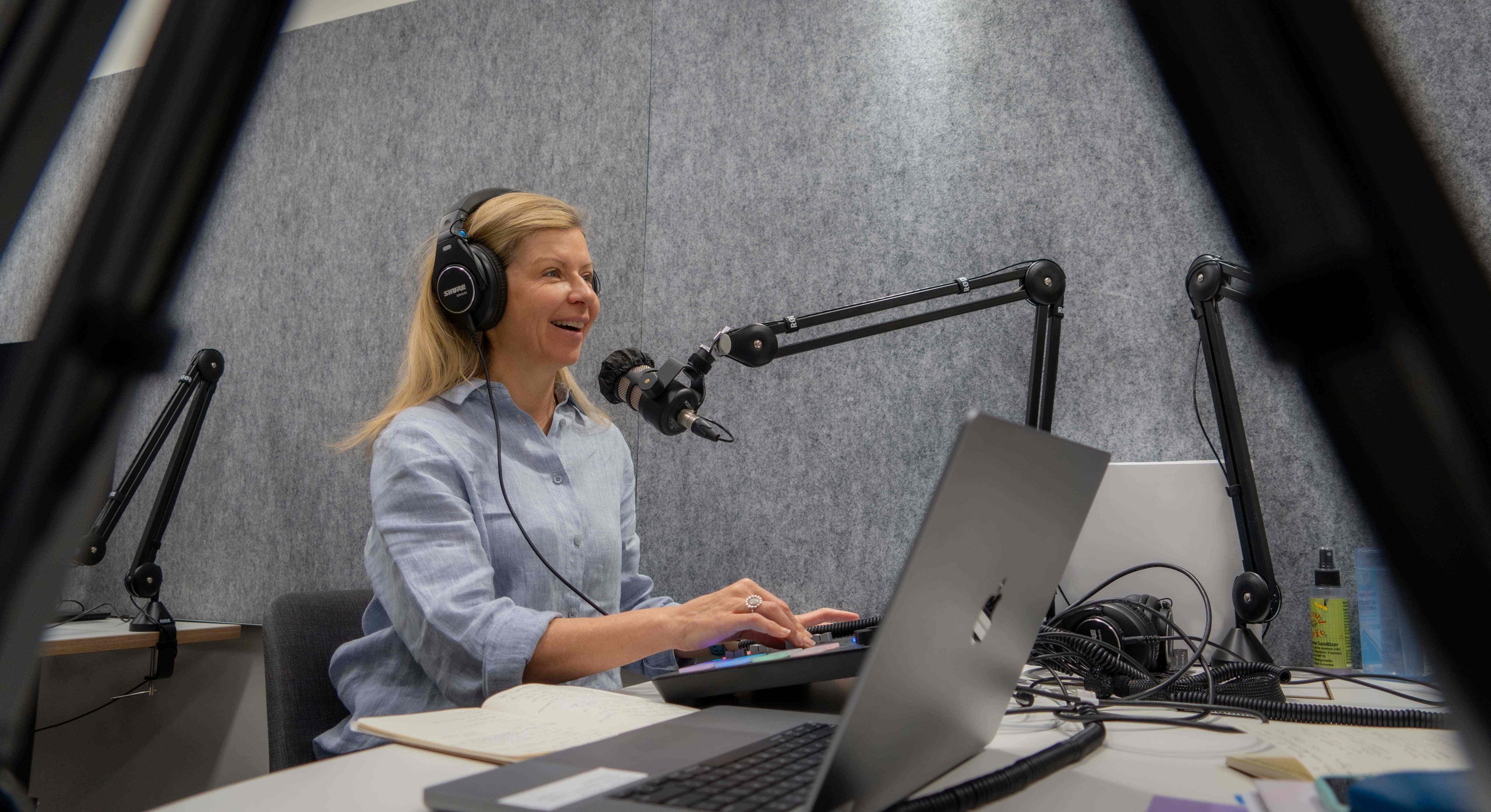 A woman speaks into a microphone while seated. She looks happy..