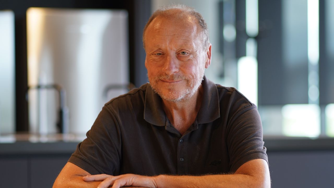 Man sits with arms crossed at table. 