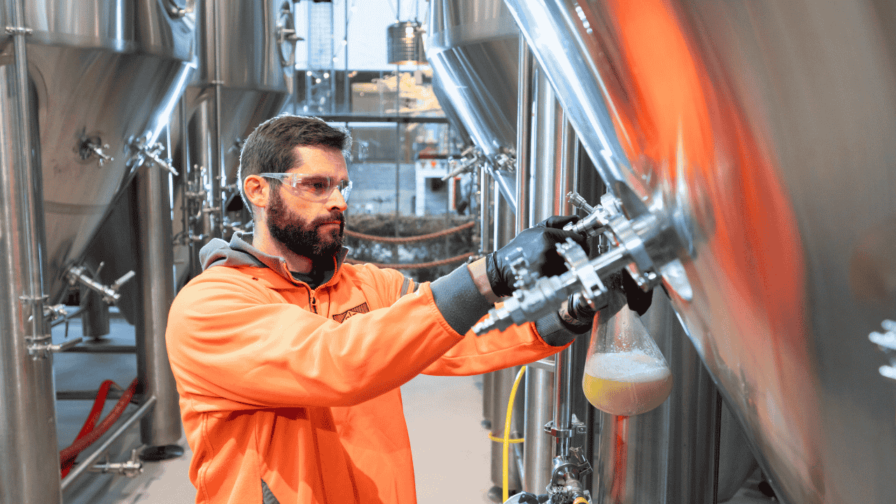 A person in protective clothing pours a liquid into a flask.