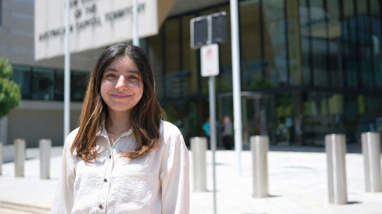 A young woman in professional clothing stands outside a court building.