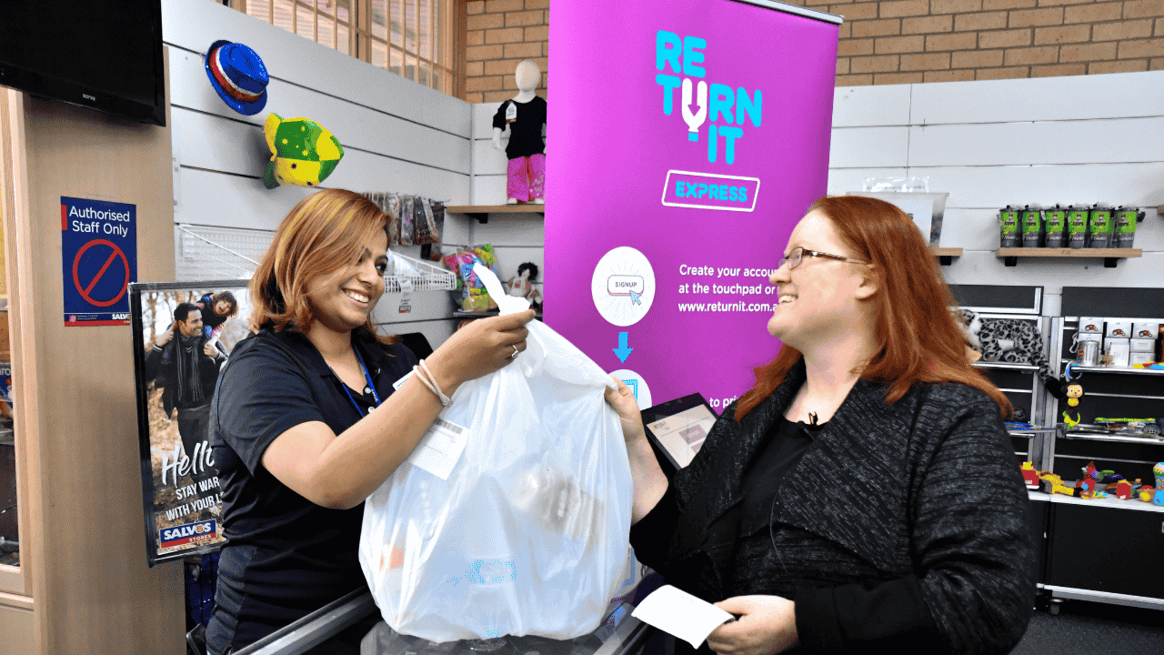A person hands another person a garbage bag filled with clothes.