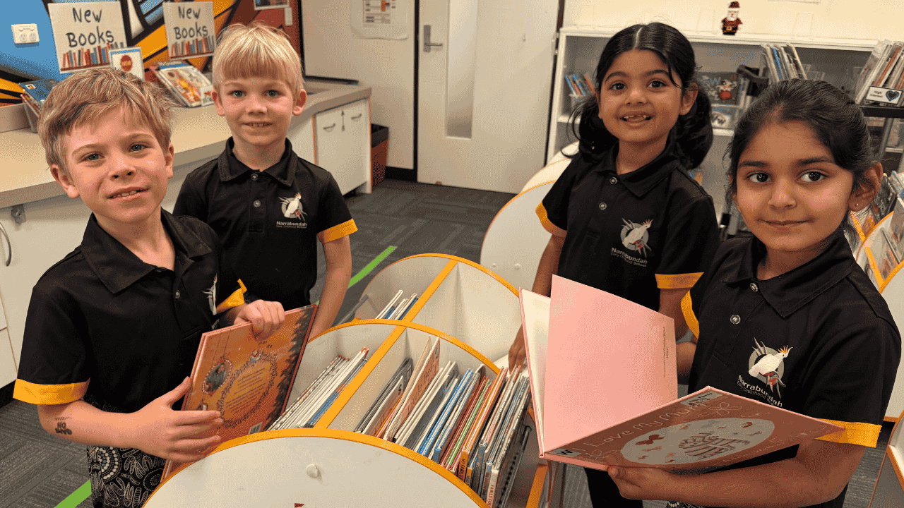 Four students hold books and smile.