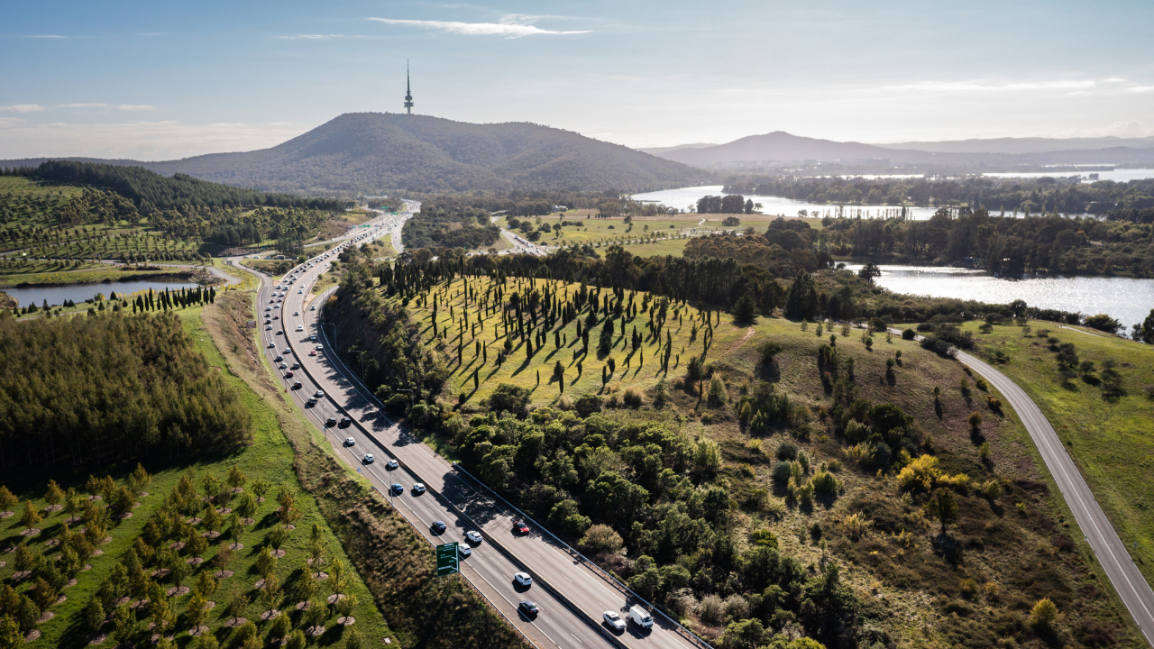 An aerial view of Canberra including the National Arboretum, a busy road, Black Mountain and the Telstra Tower