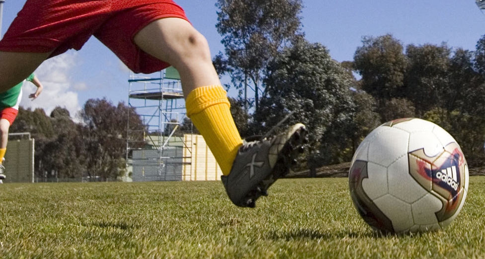A close up of a child's legs about to kick a soccer ball.