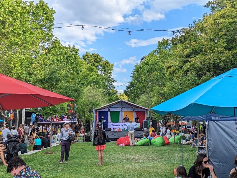 Multicultural festival taking place in City Walk with a stage and people enjoying a lovely day lounging on the grass