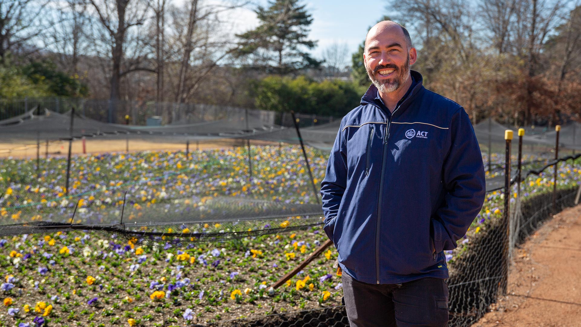 Man stands and smiles in front of colourful garden bed. 