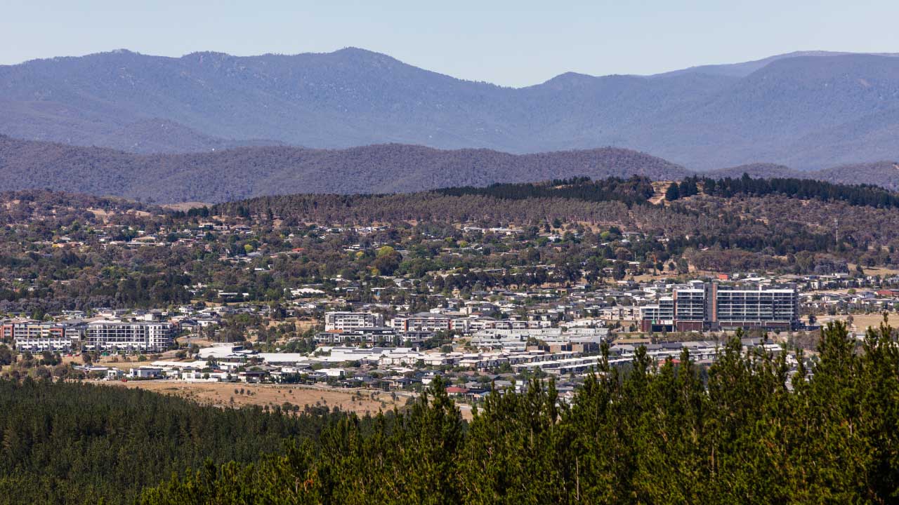 An overhead photo of a new suburb with housing surrounded by bushland and mountains.