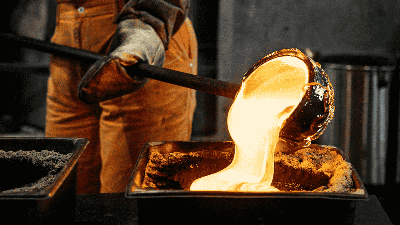 A close-up view of molten glass glowing bright orange-white as it is poured from a metal blowpipe into a sand-filled mould at Canberra Glassworks.