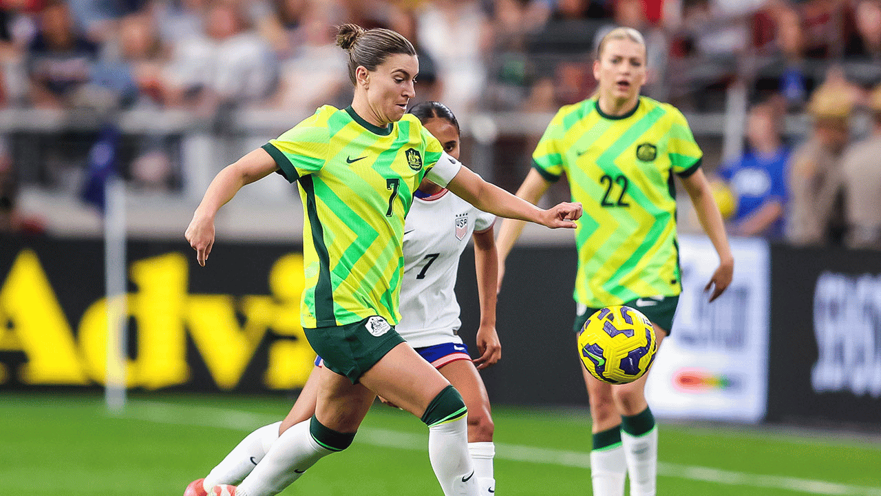 A player in a green and yellow soccer uniform controls a bright yellow ball during an international match.