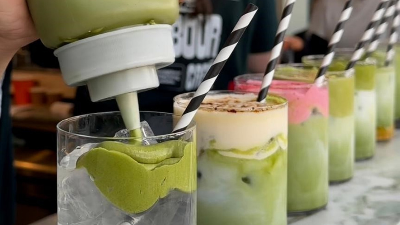 A row of iced matcha drinks sits on a marble counter, with black-and-white striped paper straws in each glass.