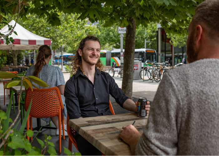 Two men sit at a table, with a woman sitting in the background. 