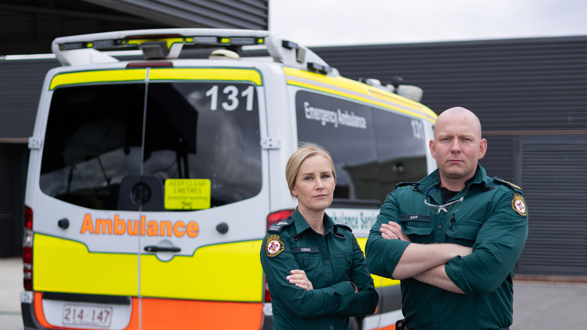 A male and female ambulance worker stand in front of an ambulance.