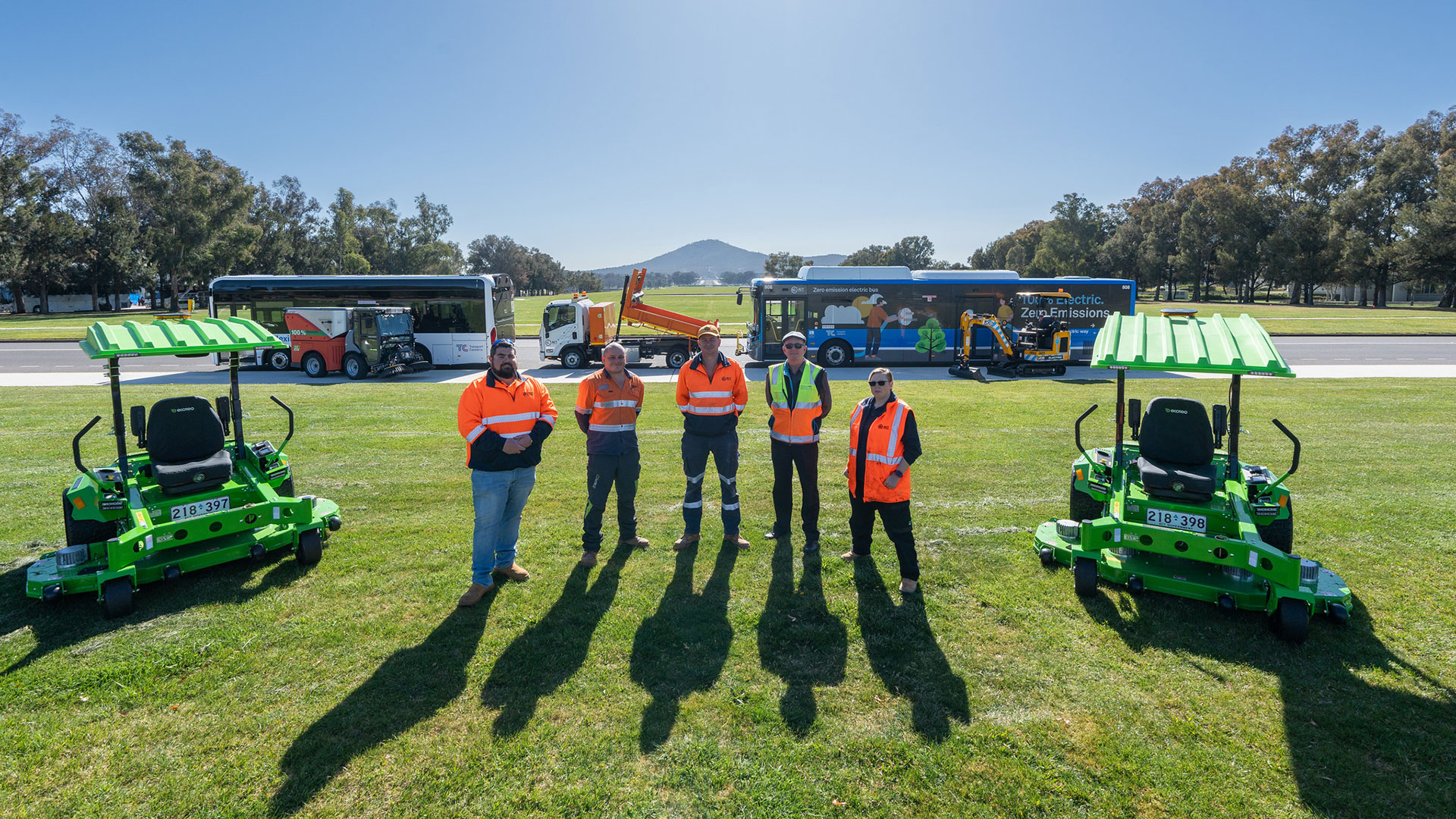 Five people stand on grass surrounded by maintenance vehicles and two buses.