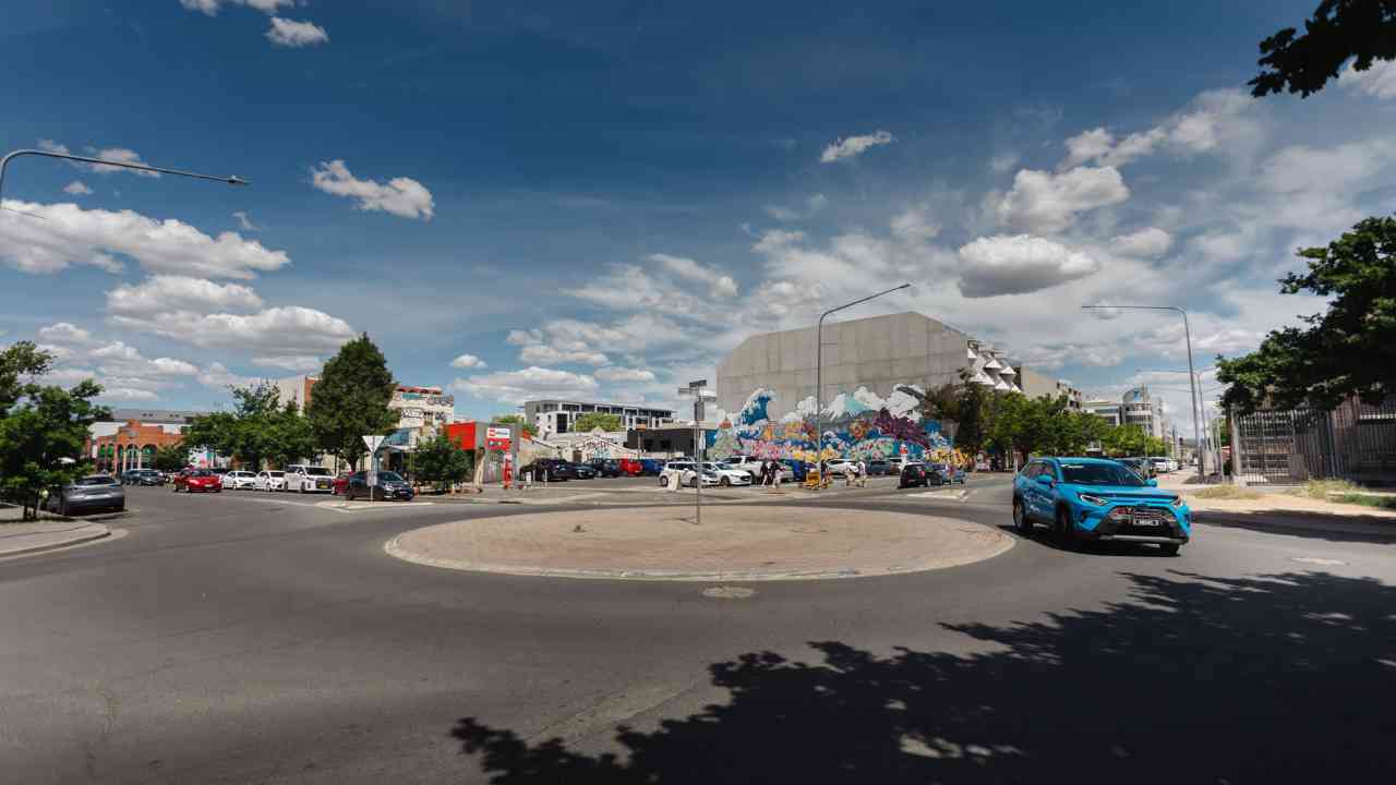 Intersection with roundabout. There is a blue car on the right driving around the roundabout.