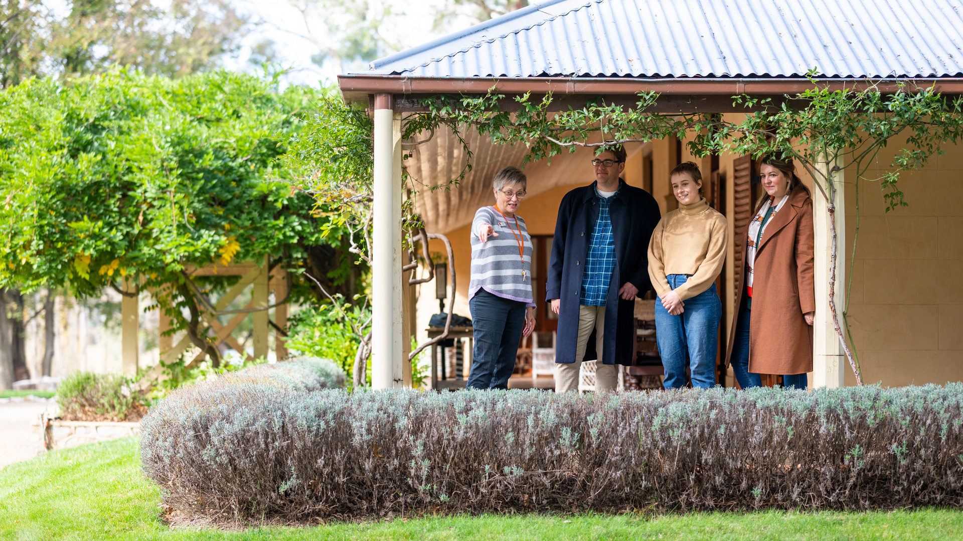 Four people stand on the deck of a heritage home.