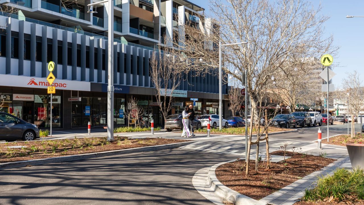 Two people using pedestrian crossing on Lonsdale Street surrounded by garden beds. 