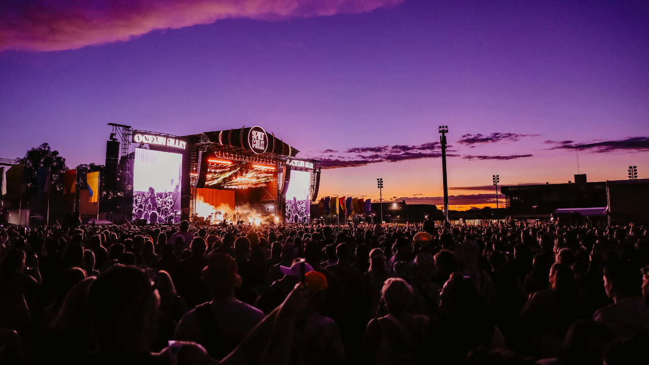 A stage with a large crowd facing it at sunset.