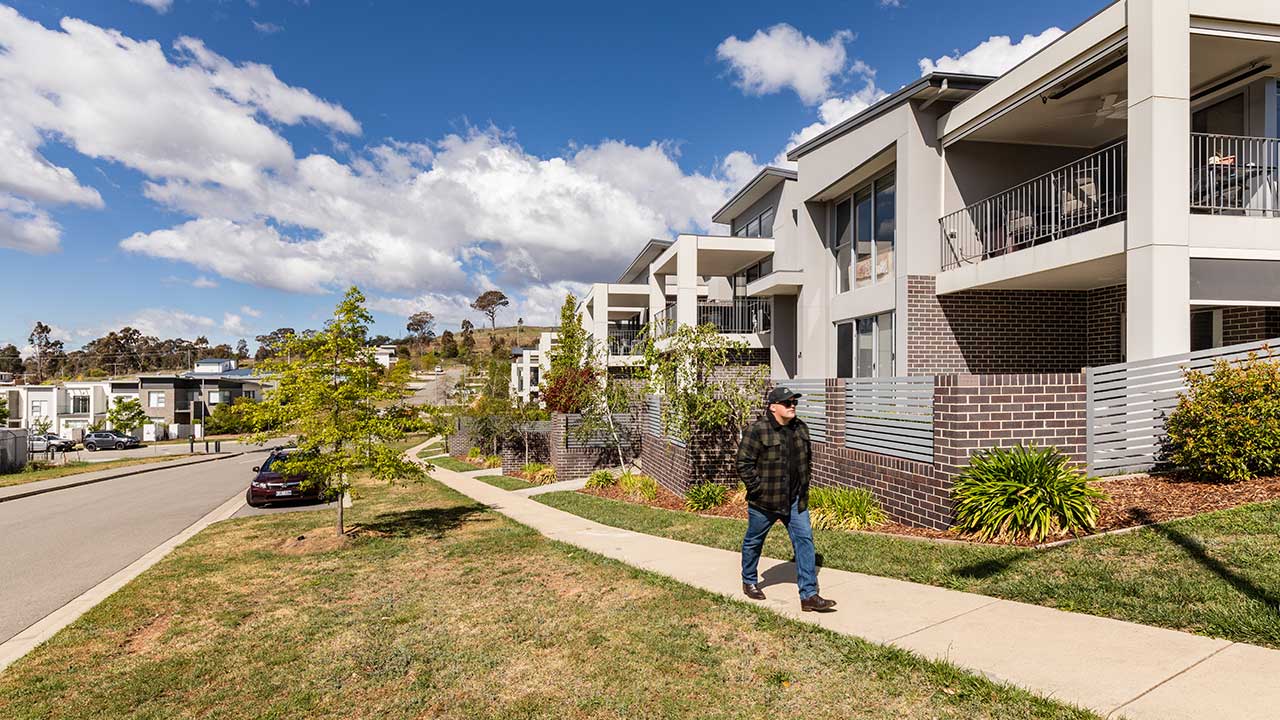 A man walks along a footpath on a street lined with modern townhouses.
