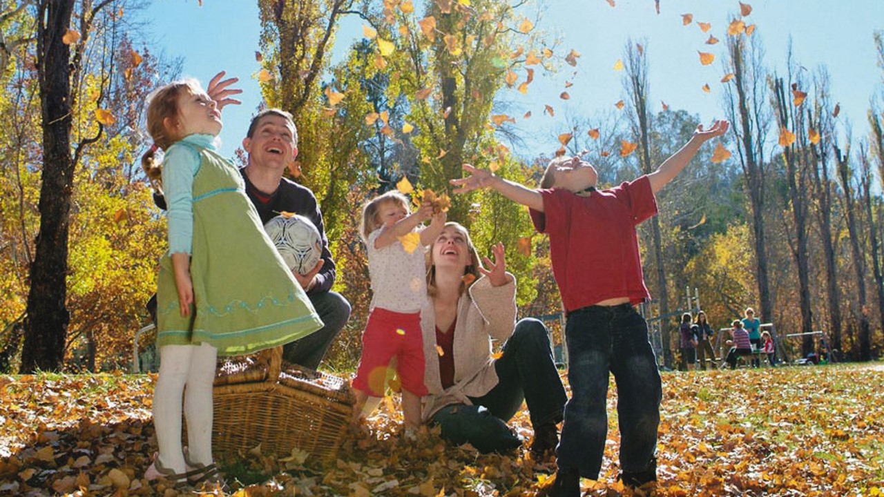 Picture of a parent and children throwing leaves into the air celebrating warm weather