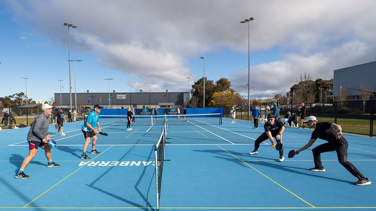 Men playing pickleball on blue outdoor courts.