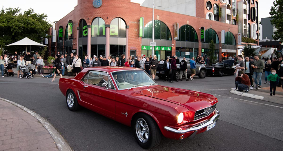 A red car drives past a crowd of spectators
