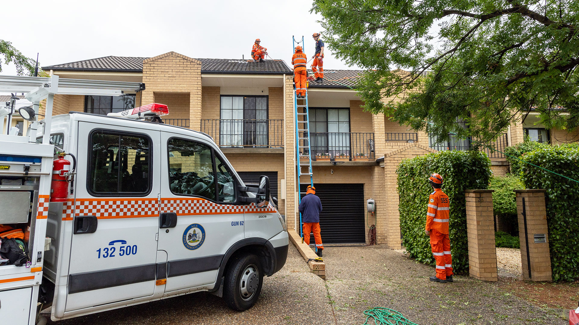 People in high-visibility clothing work on the roof of the house. There is also a ladder and truck.