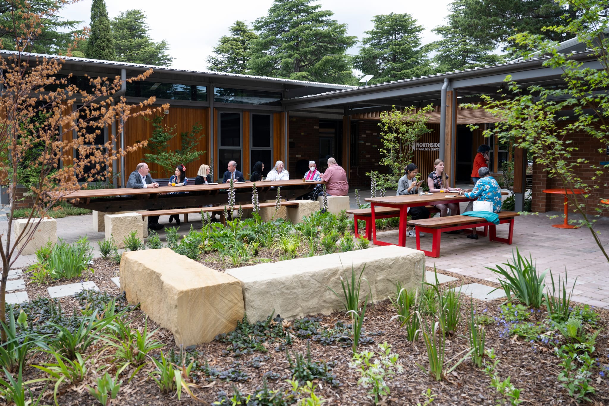 People sitting at tables and chairs amongst the gardens at Salthouse Community Centre