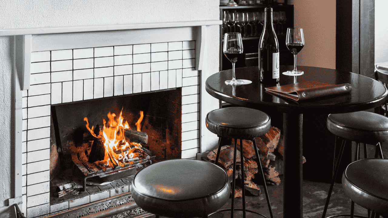 A fireplace in a restaurant with a bottle of wine and two glasses on a table.
