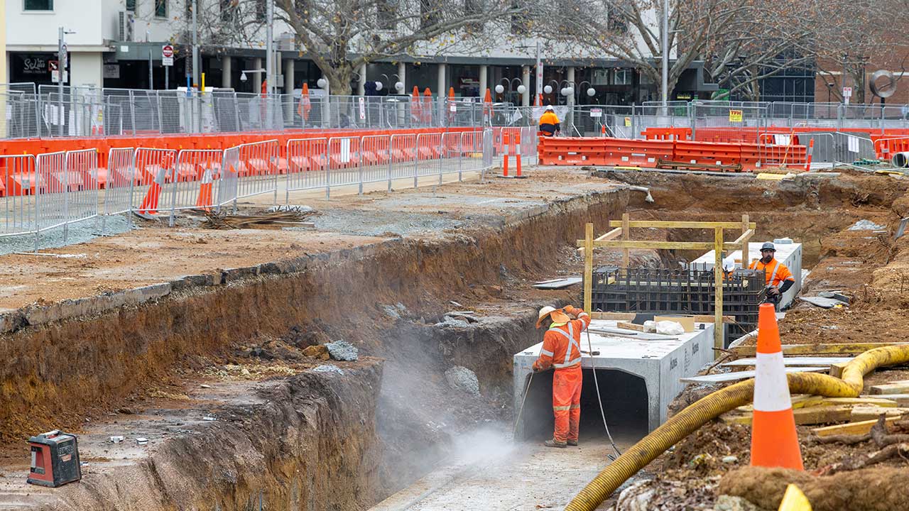 Workers in high-visibility clothing work below ground in a city construction site.