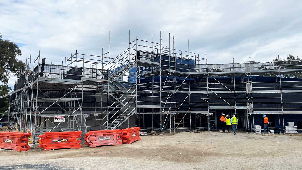 The steel frame of a building under construction, with tradespeople in high-visibility.