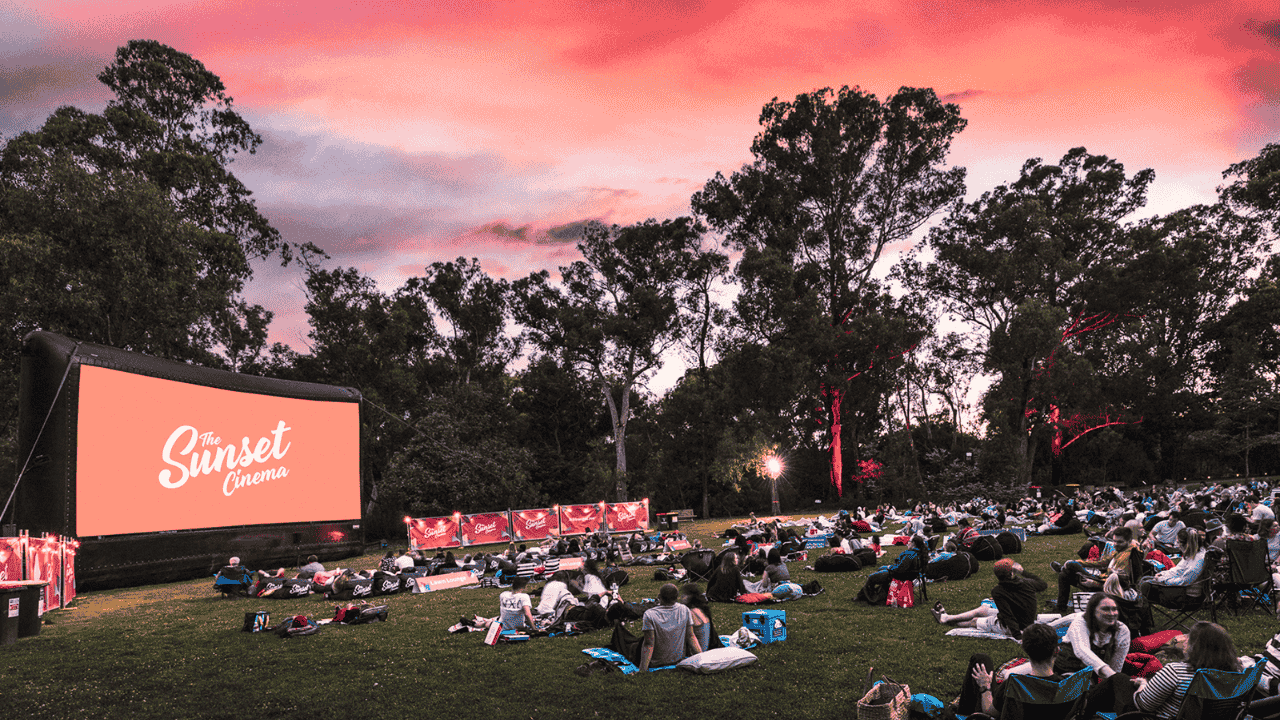A TV screen outdoors with people watching on grass lawns.