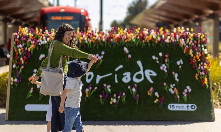 Mother with two children in front of decorated Floriade sign at light rail station. 