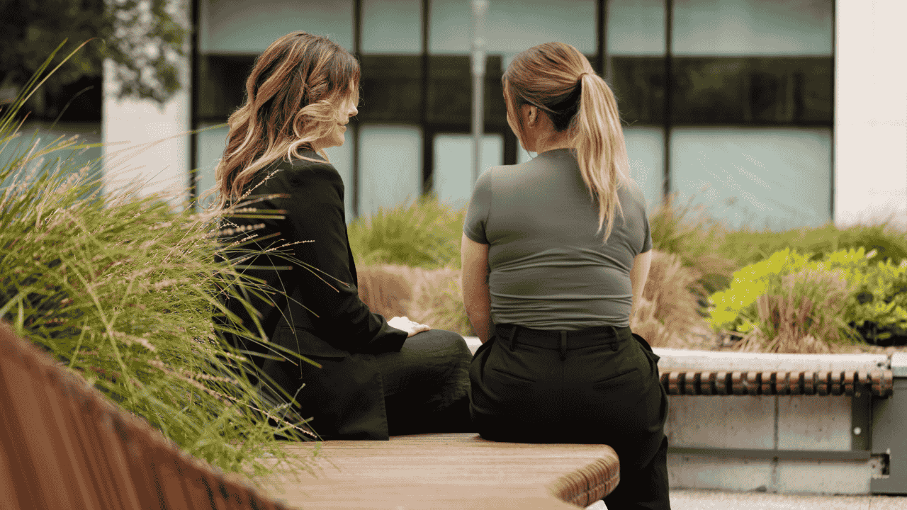Two people sit on outdoor seating talking to each other.