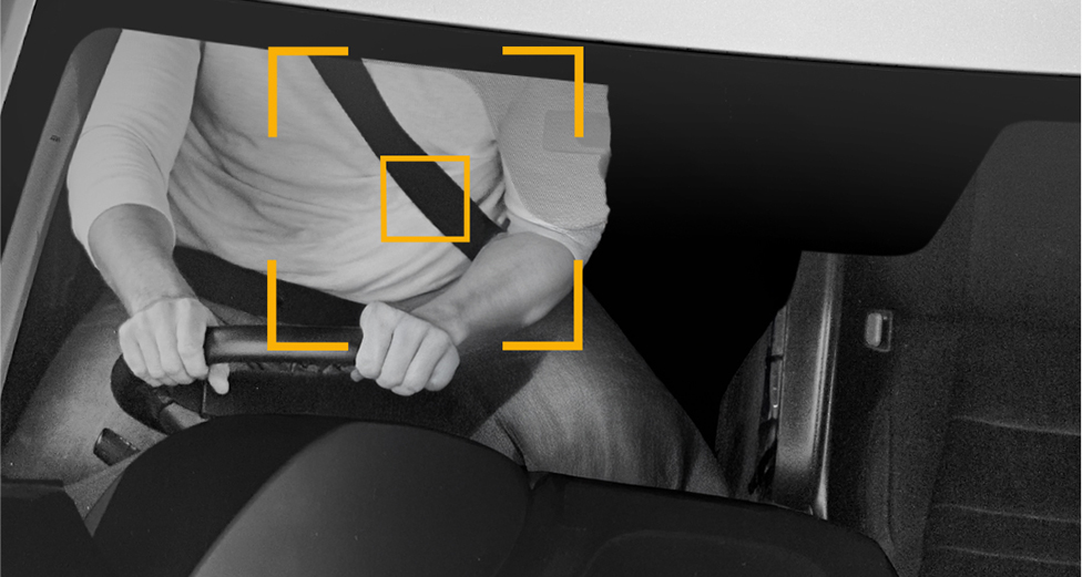 A black and white picture of someone driving a car. There are yellow lines focusing on the person's seatbelt.