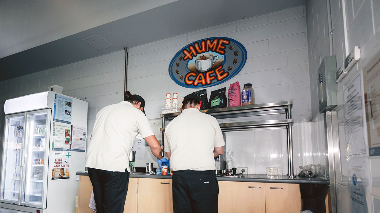 Two young men in black and white uniforms prepare drinks in a cafe. The photo is taken from behind.