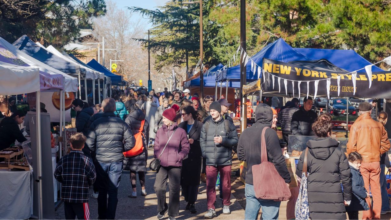 Crowds of people walk through market stalls. 