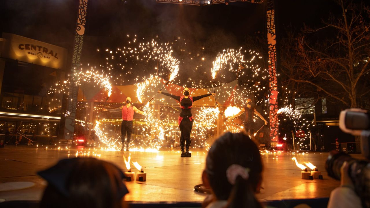 Three performers on stage with fireworks and flames, nighttime show.