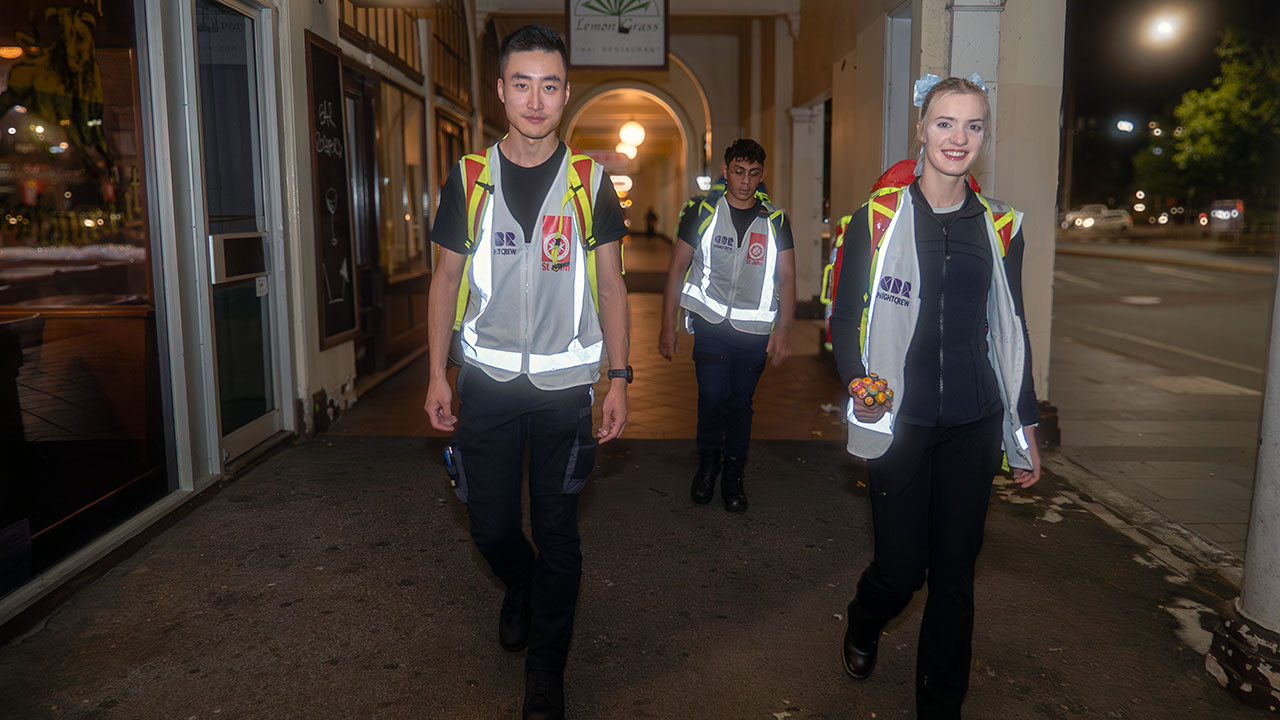 Three people in high-vis walk through the city at night.