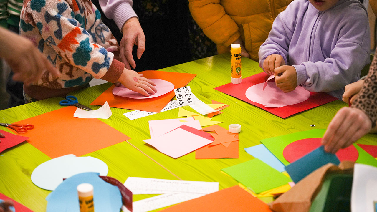 Young children working with brightly coloured cardboard around a table. The image is zoomed in so the children's faces cannot be seen.