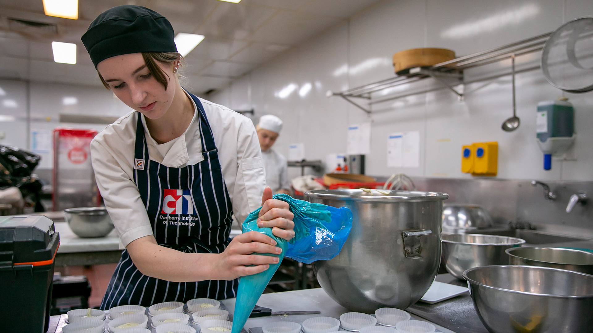 A young woman holds a piping bag in a commercial kitchen.